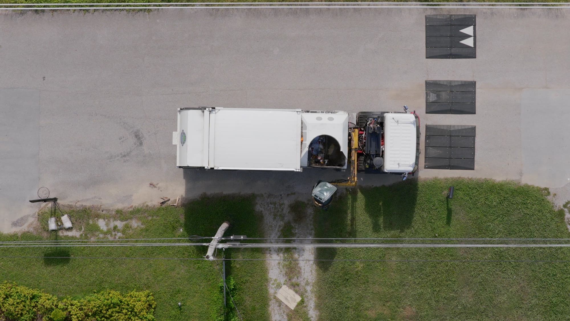 A refuse truck seen from above on a road beside a strip of grass