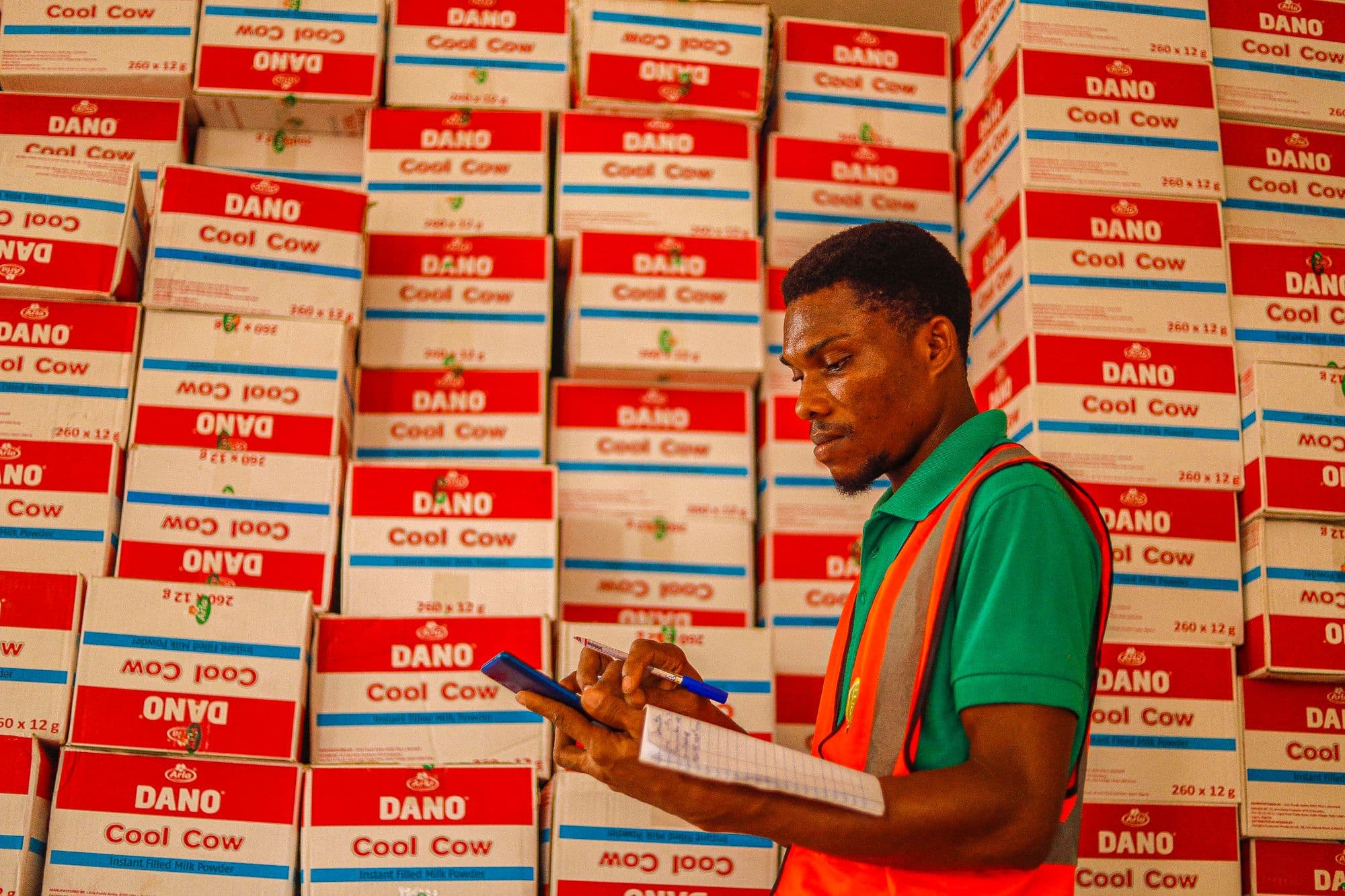 A warehouse worker in a high-visibility vest counting stacked cartons of stock