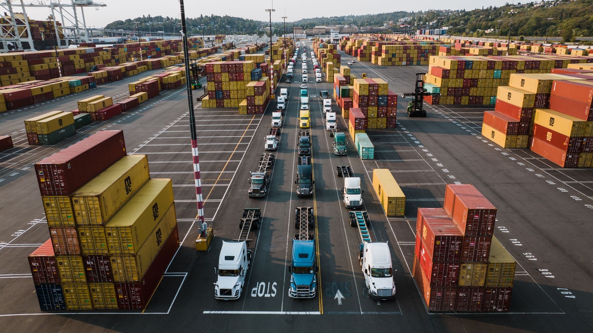 Trucks queueing between stacks of shipping containers at a port terminal